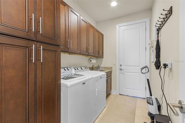 laundry area featuring light tile patterned floors, cabinet space, a sink, separate washer and dryer, and baseboards