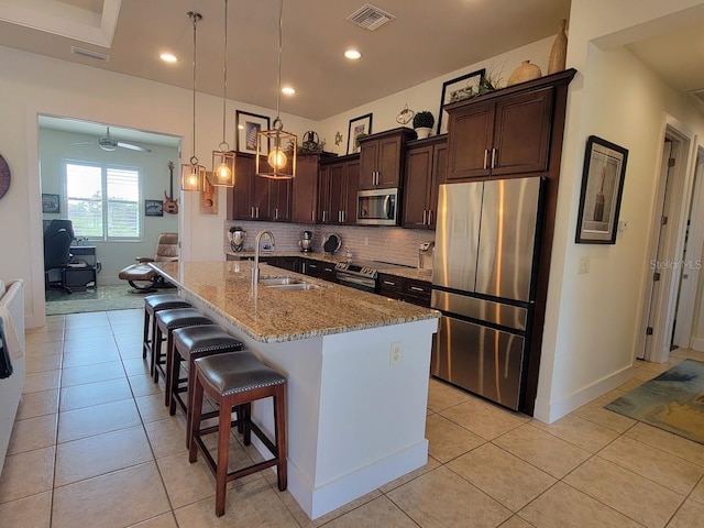 kitchen with stainless steel appliances, decorative backsplash, light tile patterned flooring, a sink, and dark brown cabinets