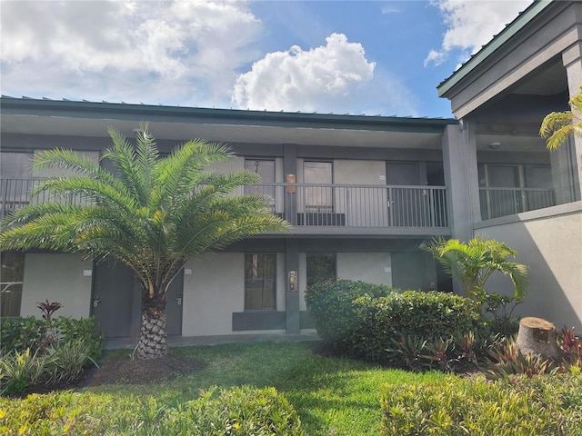 rear view of house with stucco siding, a lawn, and a balcony