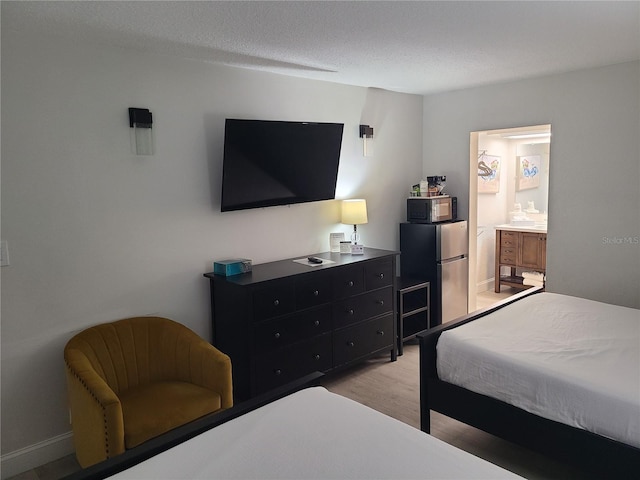 bedroom featuring light wood-type flooring, a textured ceiling, ensuite bathroom, and freestanding refrigerator