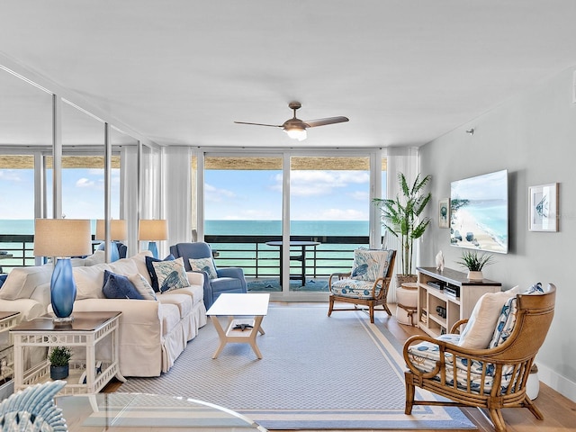 living area featuring a water view, expansive windows, a ceiling fan, and wood finished floors