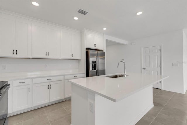 kitchen featuring light tile patterned floors, stainless steel fridge, visible vents, white cabinets, and a sink