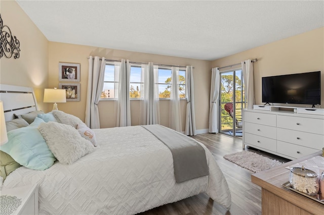 bedroom featuring access to outside, a textured ceiling, baseboards, and wood finished floors