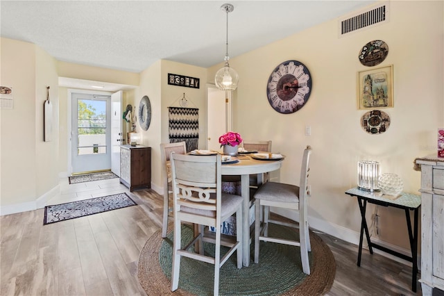 dining space with baseboards, a textured ceiling, visible vents, and wood finished floors