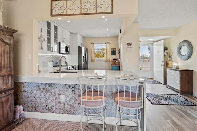 kitchen featuring a sink, white cabinetry, light countertops, appliances with stainless steel finishes, and glass insert cabinets