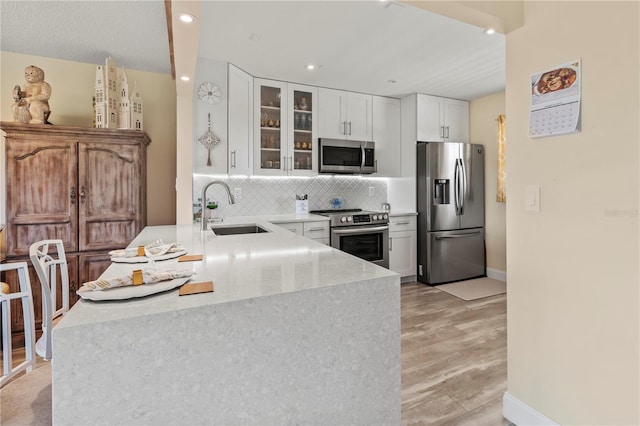 kitchen featuring a sink, tasteful backsplash, appliances with stainless steel finishes, a peninsula, and light countertops