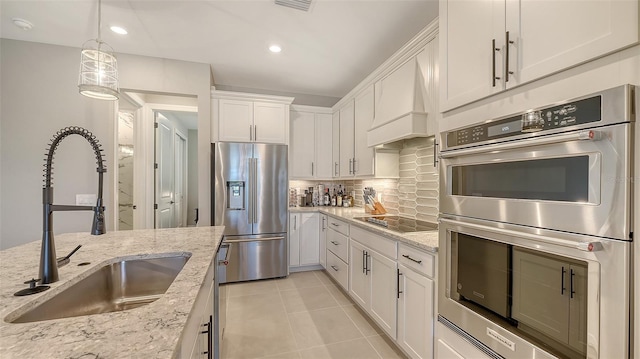 kitchen with stainless steel appliances, a sink, white cabinets, decorative backsplash, and custom range hood