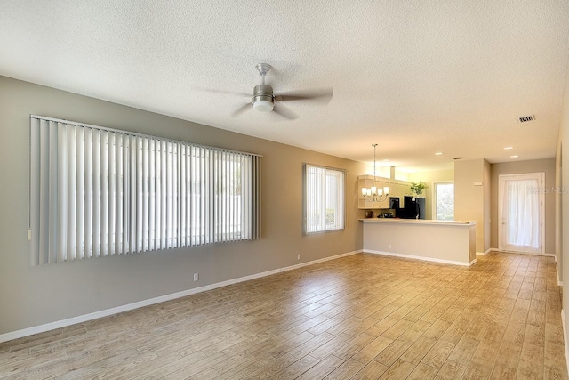 unfurnished living room featuring visible vents, light wood-style floors, a textured ceiling, baseboards, and ceiling fan with notable chandelier