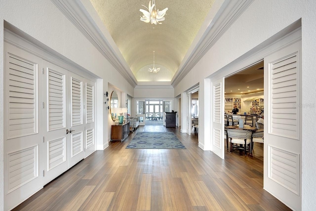 entryway with an inviting chandelier, dark wood-type flooring, ornamental molding, vaulted ceiling, and baseboards