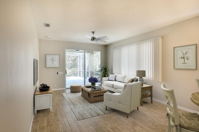 living area with a textured ceiling, baseboards, visible vents, and light wood-style floors
