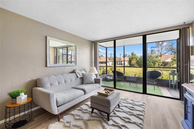 living room with baseboards, light wood-type flooring, a textured wall, expansive windows, and a sunroom