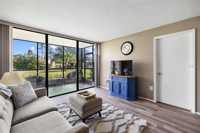 living room with light wood-type flooring, a textured ceiling, floor to ceiling windows, baseboards, and a textured wall