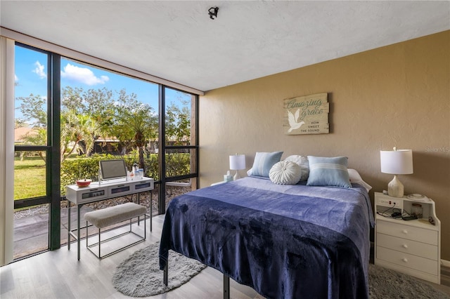 bedroom with wood finished floors, floor to ceiling windows, and a textured wall