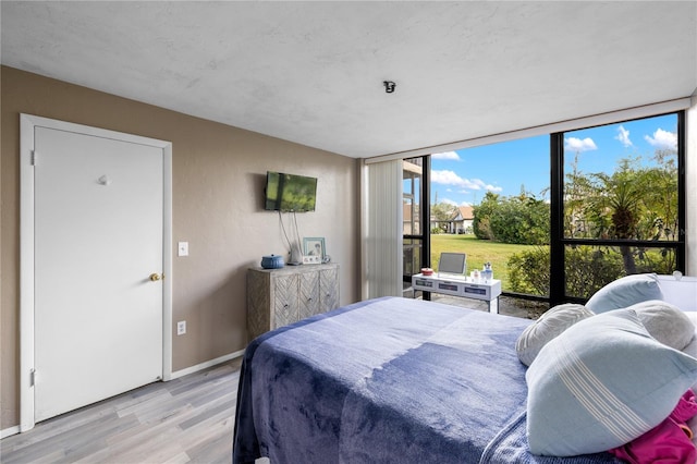 bedroom featuring floor to ceiling windows, light wood-style floors, and baseboards