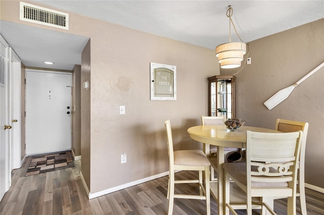 dining space featuring wood finished floors, visible vents, a textured wall, and baseboards