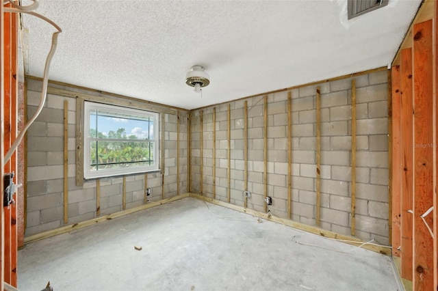 below grade area featuring concrete block wall, visible vents, and a textured ceiling