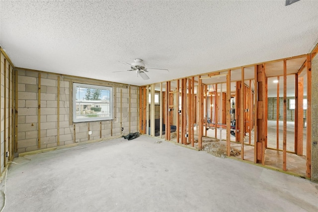 empty room with concrete block wall, ceiling fan, a textured ceiling, and concrete floors