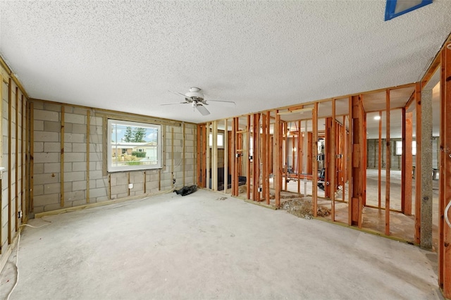 interior space featuring concrete block wall, ceiling fan, and a textured ceiling