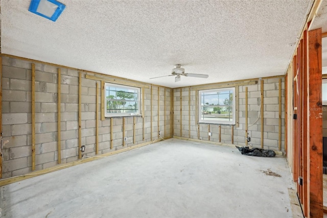 empty room featuring concrete block wall, ceiling fan, a textured ceiling, and unfinished concrete flooring