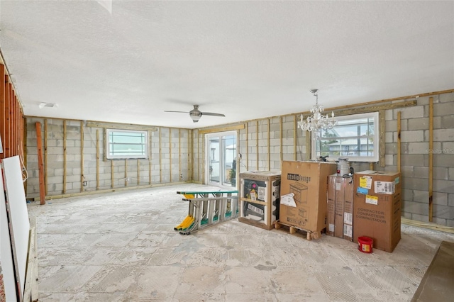 miscellaneous room featuring concrete block wall, a textured ceiling, a wealth of natural light, and ceiling fan with notable chandelier