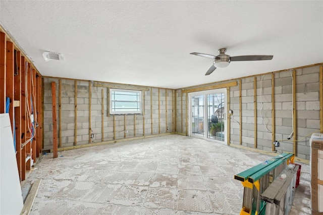 interior space with a ceiling fan, concrete block wall, visible vents, and a textured ceiling