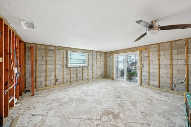 empty room featuring concrete block wall, stone finish flooring, visible vents, and a textured ceiling