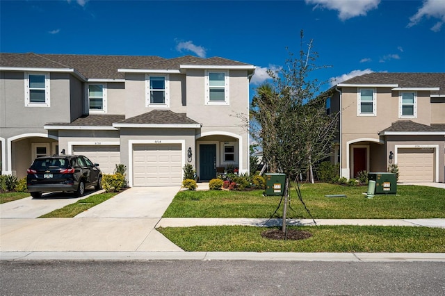 multi unit property featuring concrete driveway, roof with shingles, an attached garage, a front lawn, and stucco siding