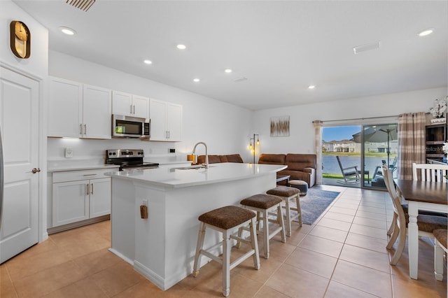 kitchen featuring appliances with stainless steel finishes, open floor plan, white cabinetry, a sink, and a kitchen breakfast bar