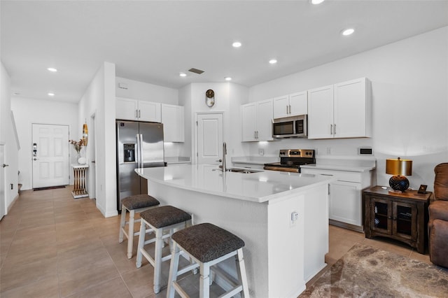 kitchen with white cabinets, appliances with stainless steel finishes, a kitchen breakfast bar, light countertops, and a sink