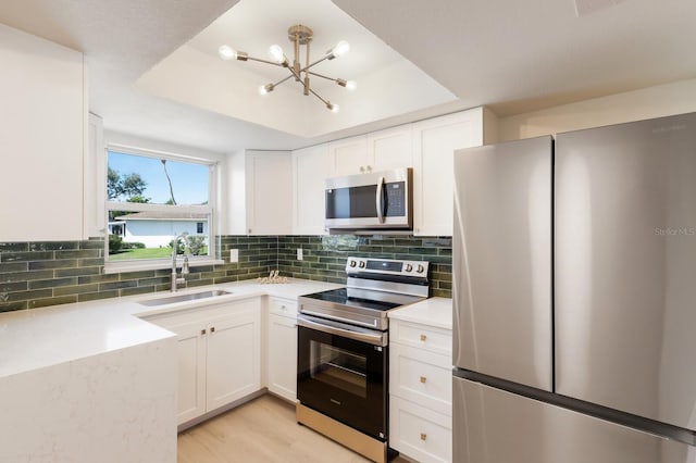 kitchen featuring a sink, appliances with stainless steel finishes, white cabinets, and a tray ceiling