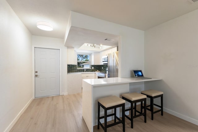 kitchen with a peninsula, light wood-style flooring, appliances with stainless steel finishes, and decorative backsplash