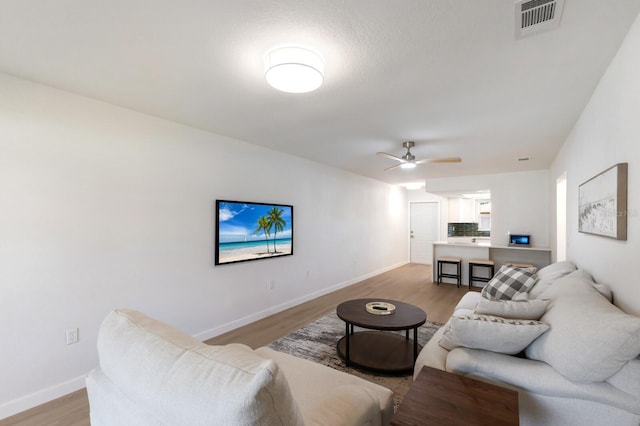 living area featuring light wood finished floors, ceiling fan, visible vents, and baseboards