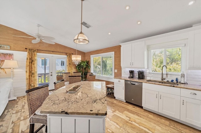 kitchen with lofted ceiling, light stone counters, stainless steel dishwasher, white cabinetry, and a sink