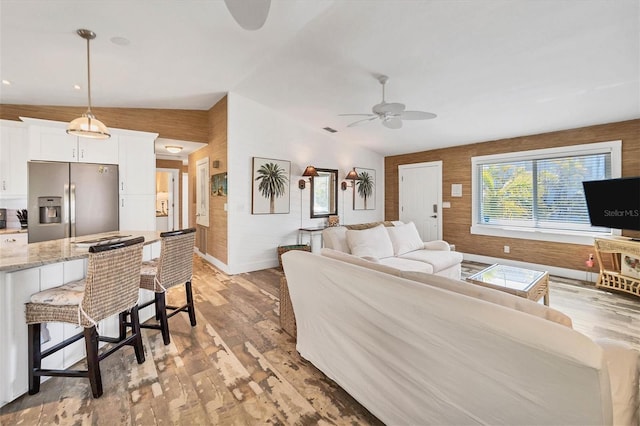 living room with visible vents, baseboards, a ceiling fan, lofted ceiling, and light wood-style floors