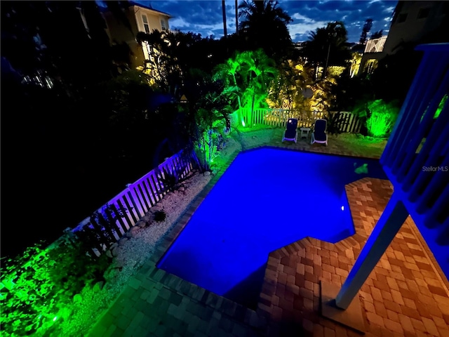 pool at night featuring a fenced backyard