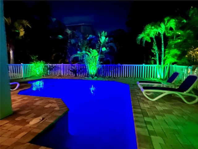 pool at night featuring a fenced backyard and a patio