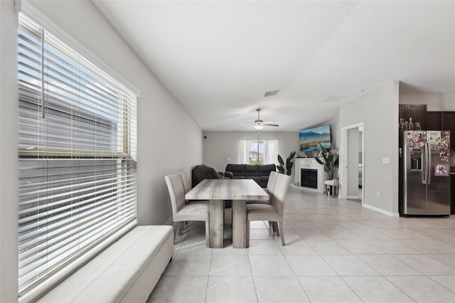 dining room with a fireplace, light tile patterned floors, visible vents, ceiling fan, and baseboards