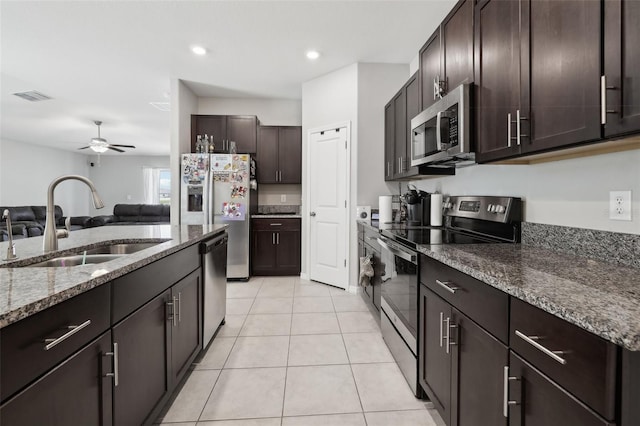 kitchen featuring light tile patterned flooring, stainless steel appliances, a sink, dark brown cabinets, and dark stone counters