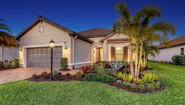 mediterranean / spanish-style house featuring a tile roof, a front yard, stucco siding, decorative driveway, and a garage