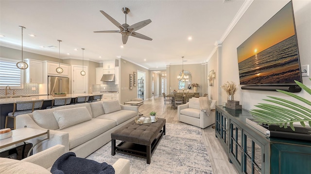 living area with recessed lighting, light wood-style flooring, ceiling fan with notable chandelier, and crown molding