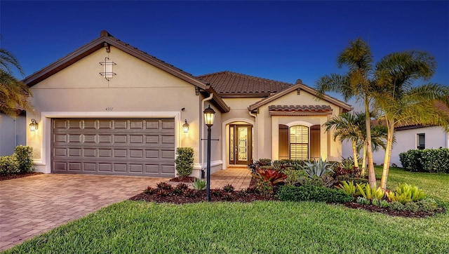 mediterranean / spanish-style house featuring a tile roof, decorative driveway, an attached garage, and stucco siding