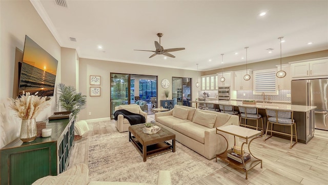 living area featuring baseboards, light wood-type flooring, ornamental molding, recessed lighting, and a ceiling fan