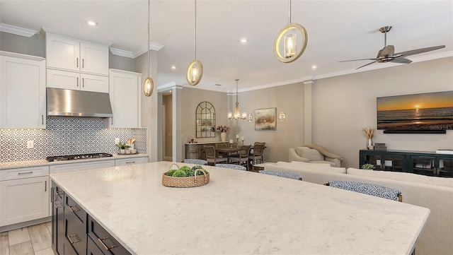 kitchen featuring under cabinet range hood, open floor plan, stainless steel gas cooktop, and ornamental molding