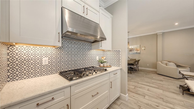 kitchen with ornamental molding, under cabinet range hood, backsplash, white cabinetry, and stainless steel gas cooktop