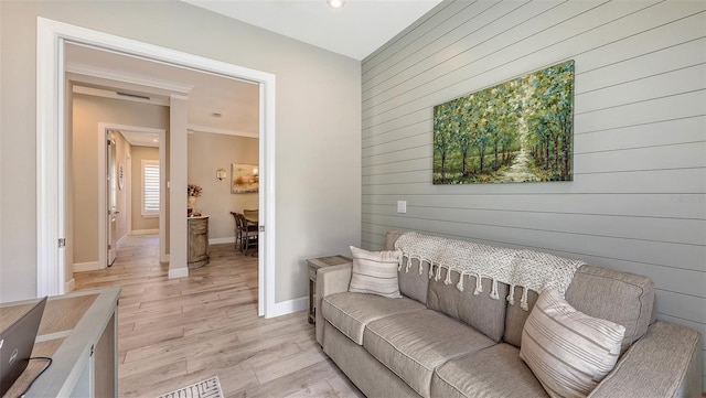 living area featuring an accent wall, wooden walls, baseboards, and light wood-type flooring