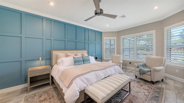 bedroom with visible vents, ornamental molding, light wood-style floors, a decorative wall, and ceiling fan