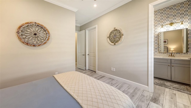 bedroom featuring light wood-type flooring, ornamental molding, a sink, connected bathroom, and baseboards