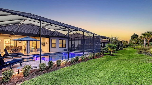 pool at dusk with glass enclosure, a patio, a yard, and an outdoor pool