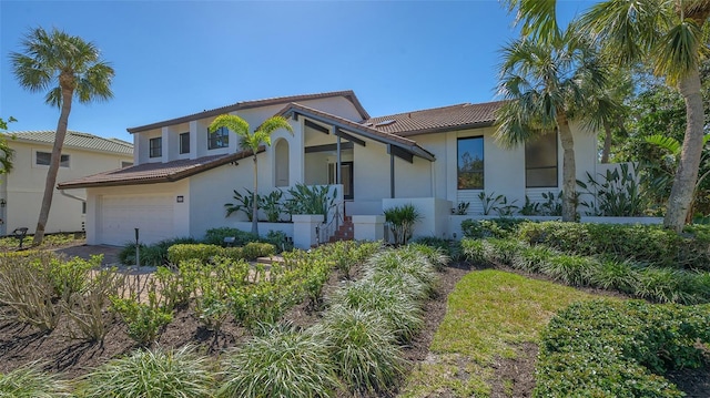 mediterranean / spanish-style house featuring a garage, a tiled roof, and stucco siding