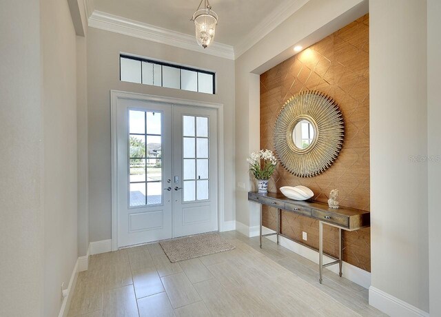 foyer with an accent wall, baseboards, crown molding, and french doors